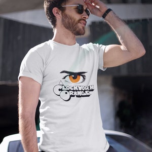 K&ouml;nnte beinhalten: Ein wei&szlig;es T-Shirt mit einer schwarz-wei&szlig;en Grafik eines Auges mit einer orangefarbenen Iris und dem Text "Clockwork Orange".
