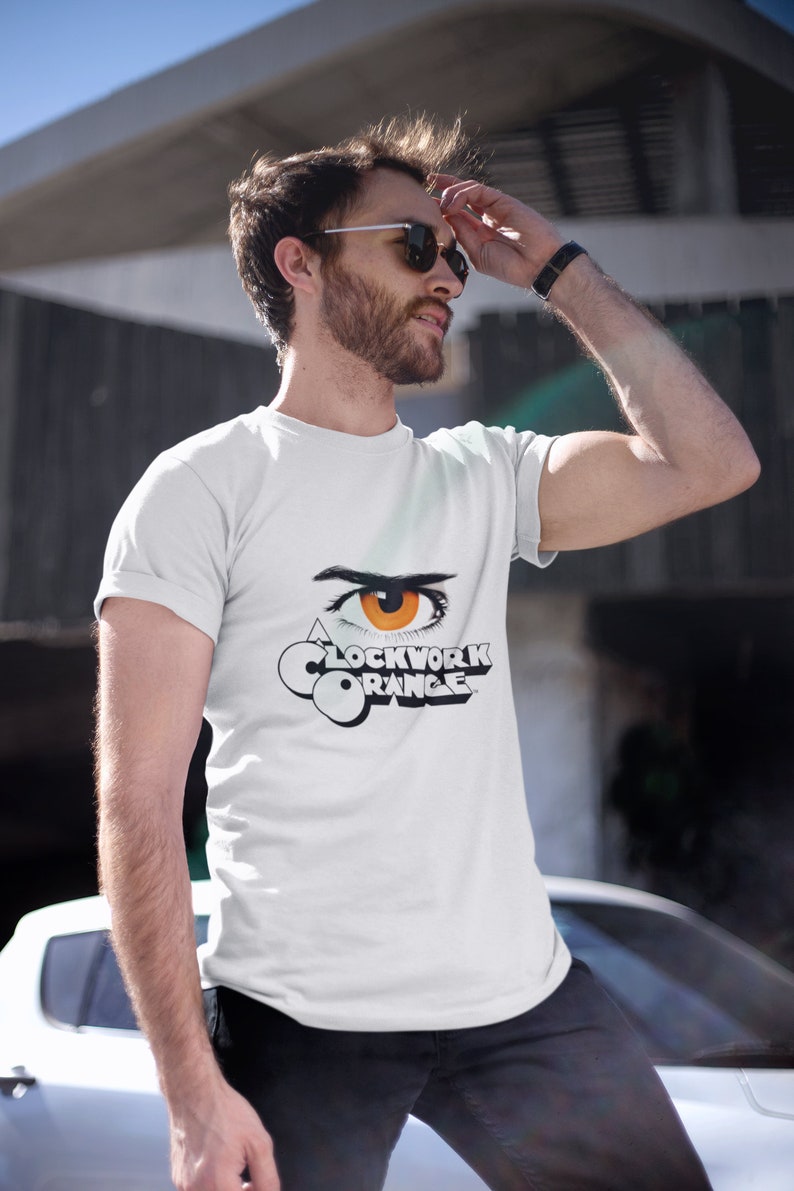 K&ouml;nnte beinhalten: Ein wei&szlig;es T-Shirt mit einer schwarz-wei&szlig;en Grafik eines Auges mit einer orangefarbenen Iris und dem Text "Clockwork Orange".