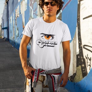 K&ouml;nnte beinhalten: Wei&szlig;es T-Shirt mit einem Aufdruck eines Auges und dem Text "A Clockwork Orange" auf der Vorderseite.