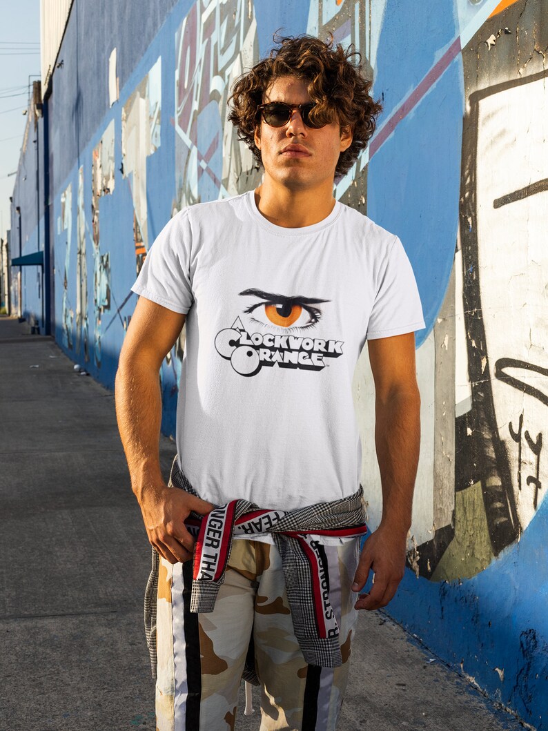 K&ouml;nnte beinhalten: Wei&szlig;es T-Shirt mit einem Aufdruck eines Auges und dem Text "A Clockwork Orange" auf der Vorderseite.