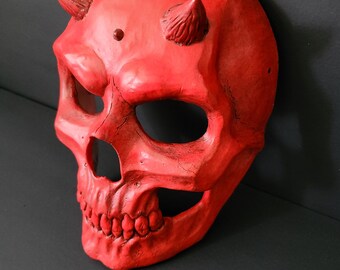 May include: A red plastic skull mask with horns. The mask has a detailed skull design with teeth and eye sockets.