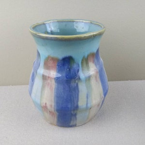 May include: A handmade ceramic vase with a light blue interior and a turquoise rim. The exterior features vertical stripes in shades of blue, white, and red. The vase has a slightly flared top and a textured surface.
