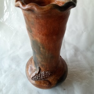 May include: A brown and black ceramic vase with a wavy rim and a carved corn design.