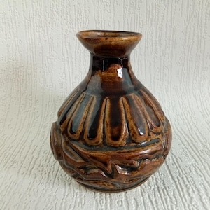 May include: A small, brown ceramic vase with a textured, ribbed design. The vase has a rounded body and a narrow neck.