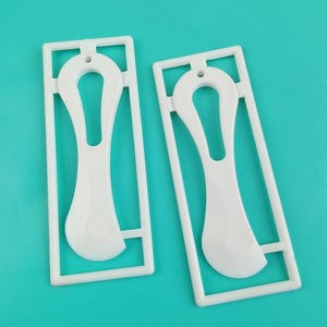 May include: Two white plastic shoe inserts with a curved design and a rectangular frame. Each insert has a hole at the top for hanging. The inserts are on a turquoise background.