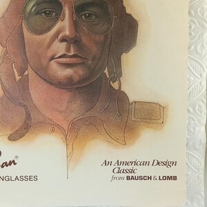 May include: Vintage advertisement featuring a portrait of a person wearing aviator sunglasses. The image is a close-up, showcasing the sunglasses and the person's face. The text reads "An American Design Classic from BAUSCH & LOMB".