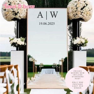 May include: A large mirror with a gold frame, displaying the initials "A | W" and the date "19.06.2025". The mirror is part of a wedding ceremony setup, with floral arrangements and seating visible.