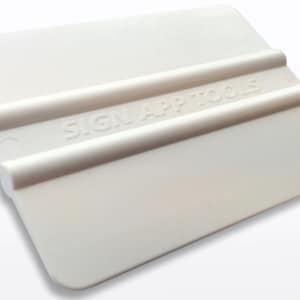 May include: A white plastic squeegee tool with the text "SIGN APP TOOLS" embossed on the surface. The tool has a rectangular shape with rounded corners and two raised ridges for grip. It is designed for applying graphics.