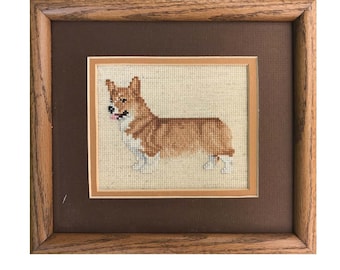 May include: A counted cross stitch chart pattern for a Pembroke Welsh Corgi. The chart is framed in a brown wooden frame and features a brown and white Corgi with a pink tongue. The chart is titled "Pembroke Welsh Corgi" and includes the text "Pegasus Originals, Inc. Counted Cross Stitch Chart" and "Chart RCFB-D".