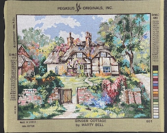 May include: A needlepoint kit featuring a cottage with a thatched roof, surrounded by lush greenery and colorful flowers. The kit includes a printed canvas, yarn, and instructions. The title of the kit is "Ginger Cottage by Marty Bell".