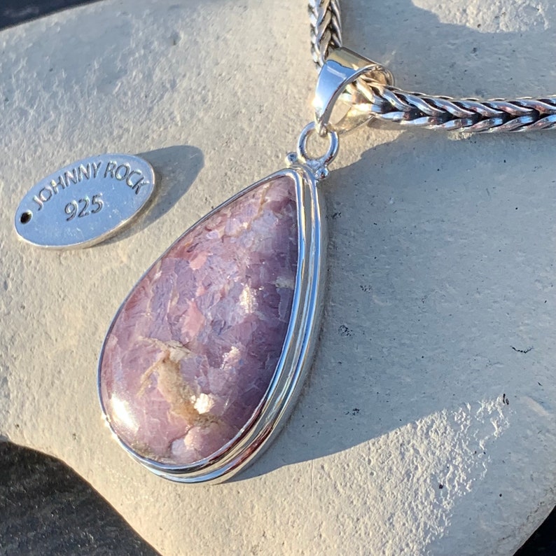 K&ouml;nnte beinhalten: Ein tropfenf&ouml;rmiger Anh&auml;nger mit einem violetten und wei&szlig;en Edelstein, der in Sterlingsilber gefasst ist. Der Anh&auml;nger ist an einer silbernen Kette befestigt. Das Etikett lautet "Johnny Rock 925".