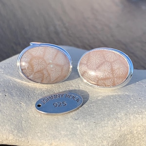 Puede incluir: Un par de gemelos de plata con una incrustación de coral fosilizado rosa claro. Los gemelos son de forma ovalada y tienen un acabado liso y pulido. La incrustación de coral presenta un patrón delicado e intrincado. Los gemelos están acompañados de una pequeña etiqueta de plata que dice "JOHNNY ROCK 925".