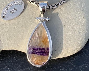 May include: A teardrop-shaped pendant with a silver frame and a colorful stone. The stone features shades of purple, orange, and clear hues. The pendant hangs from a silver chain. A small tag with the text "JOHNNY ROCK 925" is also visible.