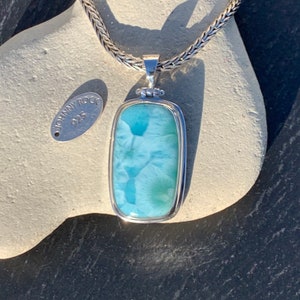 May include: A silver chain necklace with a pendant featuring a blue and green gemstone set in a silver frame. The pendant is rectangular and has a polished finish. The tag on the chain reads "Johnny Rock 925".