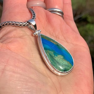 Puede incluir: Un colgante en forma de l&aacute;grima con una piedra preciosa verde y azul engastada en plata de ley. El colgante est&aacute; en una cadena de plata.
