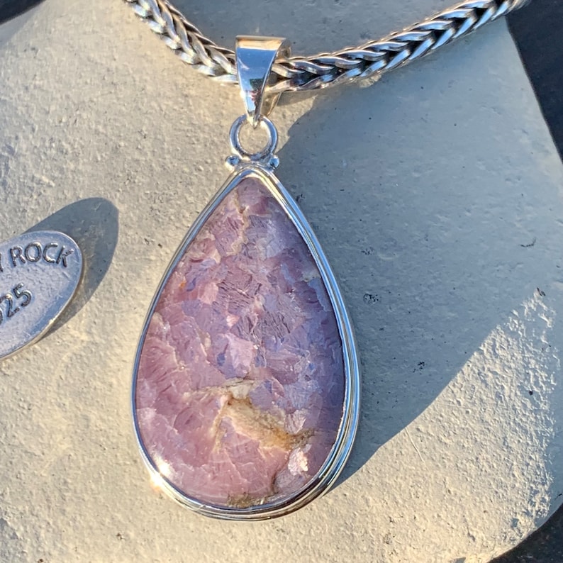 K&ouml;nnte beinhalten: Ein tropfenf&ouml;rmiger Anh&auml;nger mit einem violetten und wei&szlig;en Edelstein, der in Sterlingsilber gefasst ist. Der Anh&auml;nger h&auml;ngt an einer silbernen Kette.