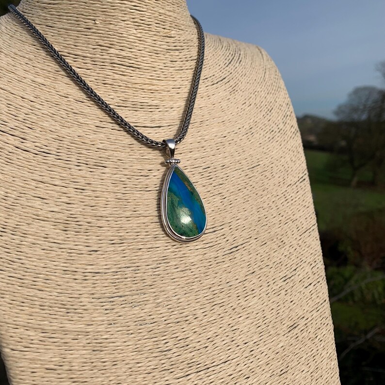 Puede incluir: Un collar de cadena de plata con un colgante en forma de l&aacute;grima con una piedra preciosa verde y azul.