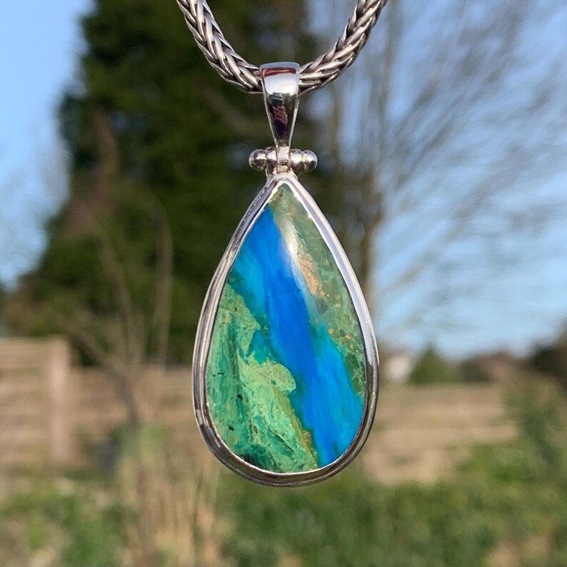 Puede incluir: Un colgante en forma de l&aacute;grima con una piedra preciosa azul y verde engastada en plata de ley. El colgante est&aacute; colgado de una cadena de plata.
