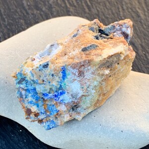 May include: A rough, irregular shaped rock with a mix of brown, white, blue, and black colors. The rock has a rough, uneven texture.