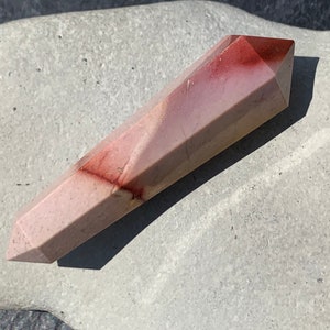 May include: A long, faceted, red and white crystal point. The crystal is polished and has a smooth, glassy finish.