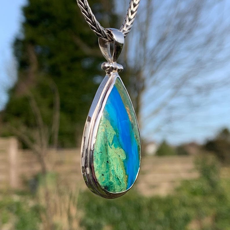 Puede incluir: Un colgante en forma de l&aacute;grima con una piedra preciosa verde y azul engastada en plata de ley.