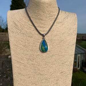 Puede incluir: Un collar de cadena de plata con un colgante en forma de l&aacute;grima con una piedra preciosa verde y azul.