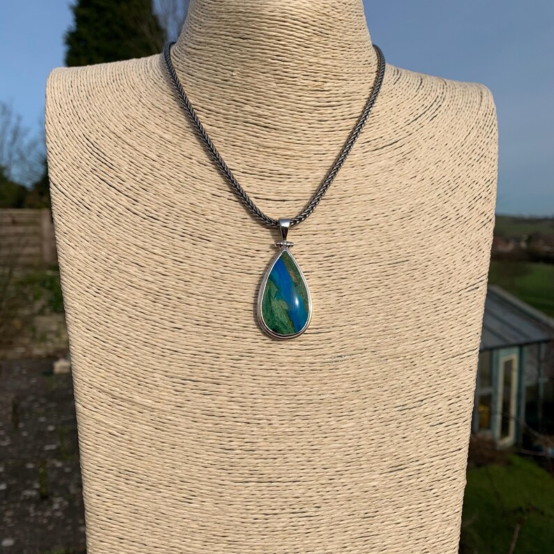 Puede incluir: Un collar de cadena de plata con un colgante en forma de l&aacute;grima con una piedra preciosa verde y azul.
