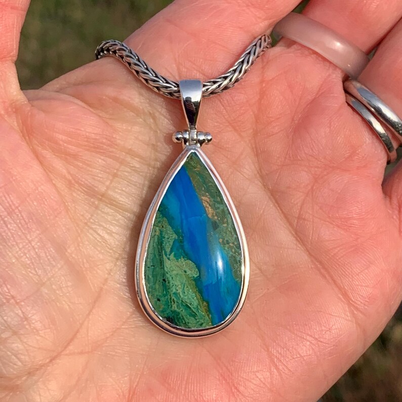 Puede incluir: Un colgante en forma de l&aacute;grima con una piedra preciosa azul y verde engastada en plata de ley. El colgante est&aacute; en una cadena de plata.