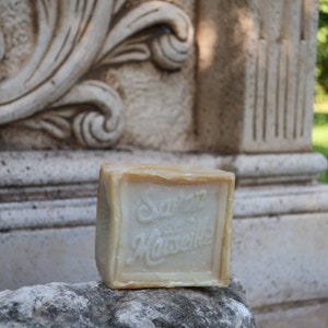 May include: A bar of soap with the words "Savon de Marseille" printed on it. The soap is sitting on a rock.