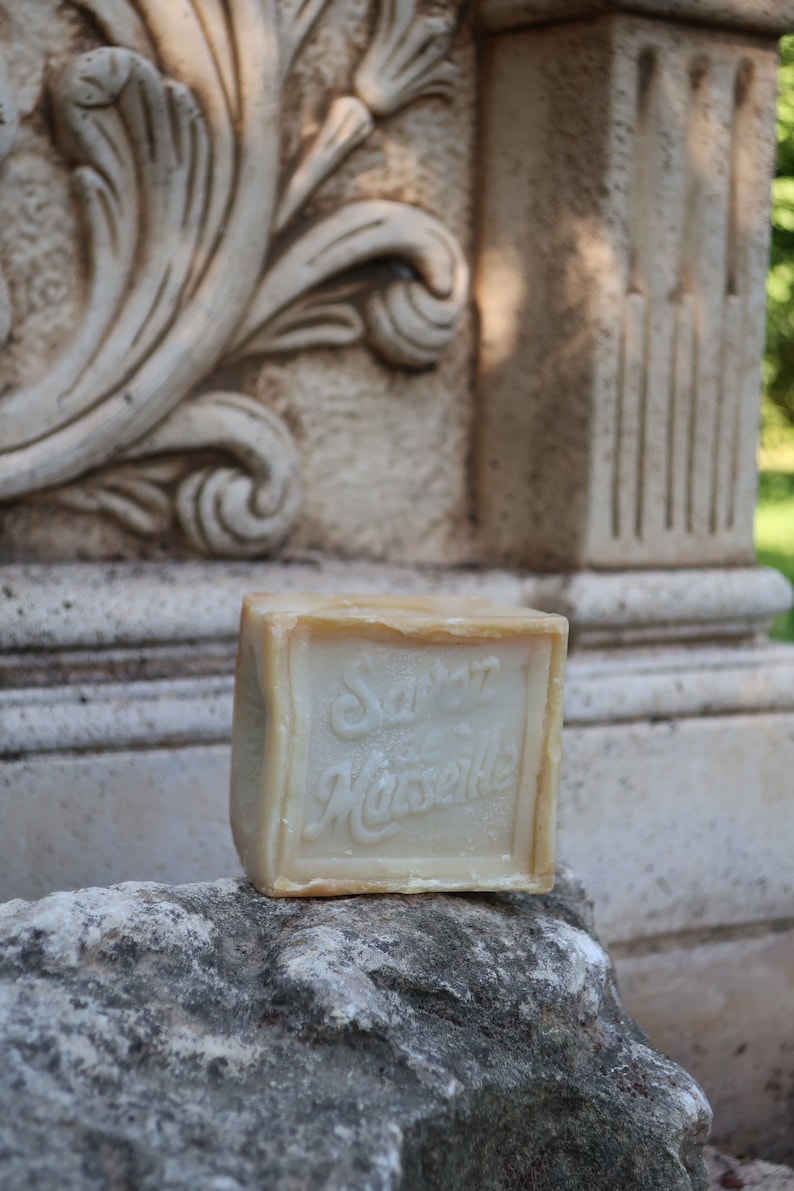 May include: A bar of soap with the words "Savon de Marseille" printed on it. The soap is sitting on a rock.