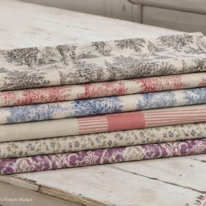 Op de afbeelding: Een stapel van zes gevouwen rechthoekige stoffen servetten met diverse patronen. Het bovenste servet heeft een zwart-wit pastoraal tafereel, gevolgd door rode en blauwe pastorale prints, een rood gestreept servet, een bloemenprint en een paars damastpatroon.