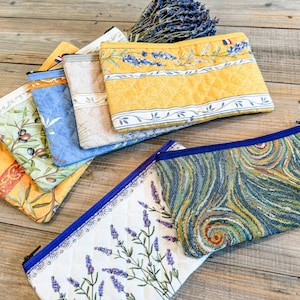 May include: Five different fabric zippered pouches with various patterns. The pouches are made of quilted fabric and feature floral, geometric, and abstract designs. The pouches are arranged in a stack on a wooden surface.