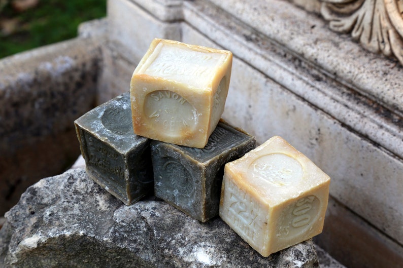 May include: Four bars of soap, two are beige and two are dark green. The beige bars have the word "Savon" printed on them.