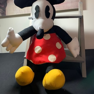 May include: A plush Minnie Mouse doll with a red dress with white polka dots, a red bow with white polka dots, and yellow shoes. The doll has black ears, arms, and legs, and a white face with black eyes and nose.