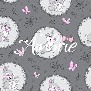 May include: A repeating pattern featuring cartoon bunnies in oval frames, with pink accents and butterflies on a grey background. The word "Amorie" is written in white script across the image. Floral and leaf elements complete the design.