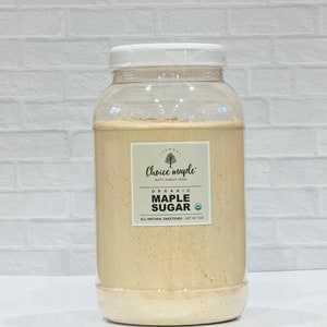 May include: A clear plastic jar filled with light brown organic maple sugar. The jar has a white lid and a white label with the text "Choice maple" and "NOTT FAMILY FARM". The label also says "ORGANIC MAPLE SUGAR" and "ALL-NATURAL SWEETENER NET WT 5LB".