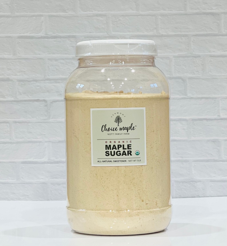 May include: A clear plastic jar filled with light brown organic maple sugar. The jar has a white lid and a white label with the text "Choice maple" and "NOTT FAMILY FARM". The label also says "ORGANIC MAPLE SUGAR" and "ALL-NATURAL SWEETENER NET WT 5LB".