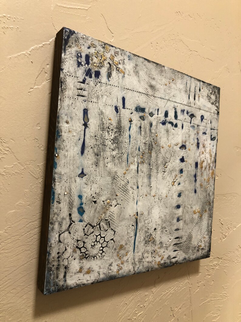 K&ouml;nnte beinhalten: Abstrakte Malerei auf Leinwand mit wei&szlig;em Hintergrund und blauen und goldenen Akzenten. Das Gem&auml;lde hat eine strukturierte Oberfl&auml;che und einen verwitterten Look.