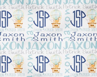 May include: A white baby blanket with a blue and white pattern of hot air balloons and the name "Jaxon Patrick Smith" repeated throughout.