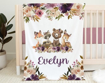 May include: A white baby blanket with a purple floral design and a watercolor illustration of a fox, raccoon, bear, and deer. The blanket has the name "Evelyn" written in purple script.
