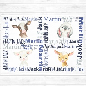 May include: A white baby blanket with the names "Martin Jack" repeated in a blue and grey pattern. The blanket features watercolour illustrations of a cow, a lamb, and a bunny.