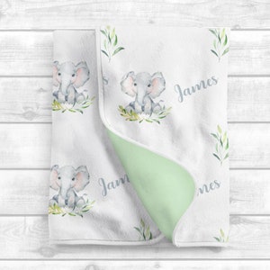 May include: A white baby blanket with a green and white elephant print. The blanket is personalized with the name "James".
