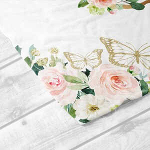 K&ouml;nnte beinhalten: Ein wei&szlig;er Stoff mit einem floralen Muster aus rosa Rosen, gr&uuml;nen Bl&auml;ttern und goldenen Glitzer-Schmetterlingen. Der Stoff ist &uuml;ber eine wei&szlig;e Holzoberfl&auml;che gefaltet.