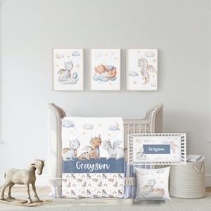 May include: A nursery set with a dragon theme, including a crib, bedding, and framed art. The set features a crib bumper, blanket, pillow, and three framed prints. The colour scheme is blue, white, and beige, with illustrations of dragons.