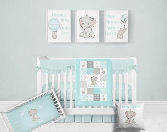 Könnte beinhalten: Ein Kinderzimmer-Set mit einem weißen Kinderbett und hellblauer Bettwäsche. Das Set enthält eine Steppdecke, ein Kissen und einen Bettschutz mit Elefantenmotiven. Drei gerahmte Drucke über dem Kinderbett zeigen Elefantenkunst und inspirierende Zitate.