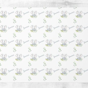 May include: White fabric with a repeating pattern of a gray elephant sitting in green grass with the name "James" written in gray script.
