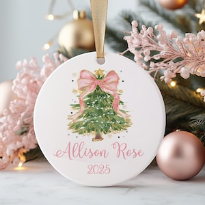 May include: White ceramic Christmas ornament with a watercolor Christmas tree design. The tree is decorated with a pink bow and lights. The name "Allison Rose" and the year "2025" are written in pink script.
