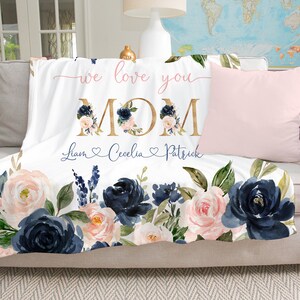 May include: White fleece throw blanket with a floral design in shades of navy blue and pink. The blanket features the text "we love you MOM" in gold lettering and the names "Liam, Cecilia, Patrick" in cursive script with hearts.