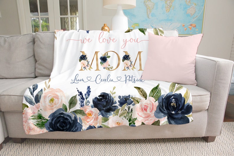 May include: White fleece throw blanket with a floral design in shades of navy blue and pink. The blanket features the text "we love you MOM" in gold lettering and the names "Liam, Cecilia, Patrick" in cursive script with hearts.