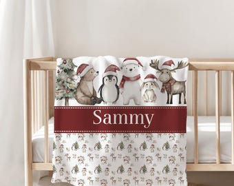 May include: A white baby blanket with a festive Christmas design. The blanket features a maroon band with the name "Sammy" in white. Above the band are illustrations of a Christmas tree, bear, penguin, polar bear, bunny, and moose, all wearing Santa hats.